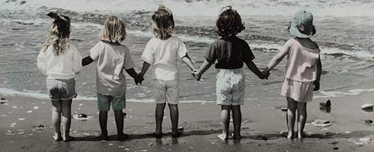 A row of children hold hands at the beach.